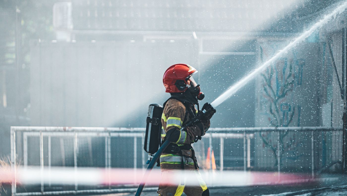 Bombeiro com equipamento de proteção praticando o uso de uma mangueira